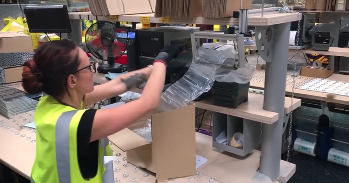 Worker using air cushion packaging machine to fill boxes